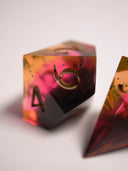 dés de JDR dégradés d'un orange chaud transparent vers un rose grenadine, vers un noir opaque brillant, aux chiffres peints couleur champagne, retro-sunset